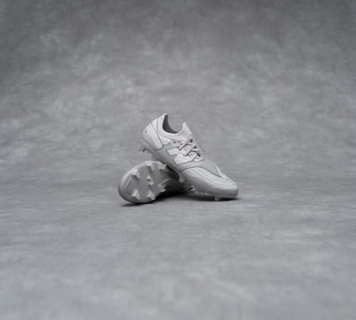 Side view of grey New Balance soccer cleats.